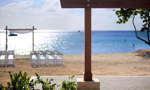 The image shows a serene beach scene, with a focus on a wooden structure in the foreground, possibly a signpost or part of a shelter