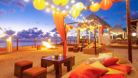 This image depicts a vibrant beachside setting at dusk, beautifully lit with a variety of lights