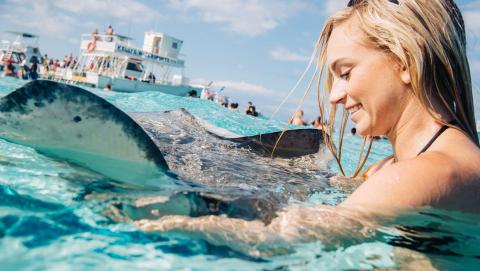 This image captures a joyful moment where a woman is interacting with a stingray in clear, shallow waters