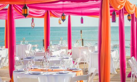 This image shows an outdoor dining setup on a wooden deck by the beach