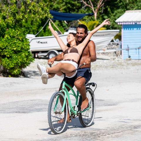 The image shows two people having fun on a bicycle in a sunny, outdoor setting