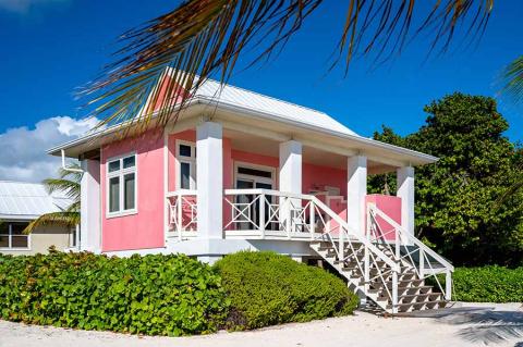 The image shows a charming pink house with a white trim located in a tropical setting
