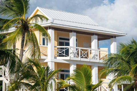 This image features a two-storey house with a tropical design, characterized by its bright yellow walls and white trim