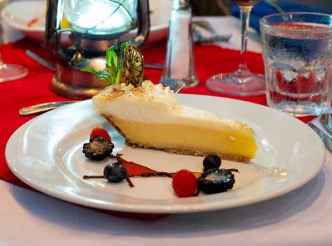 The image shows a slice of key lime pie on a white plate garnished with whipped cream and a piece of lime