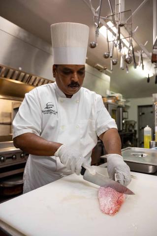 The image features a chef in a professional kitchen, focused on preparing food