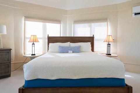 The image shows a well-lit bedroom with a neatly arranged bed at the center