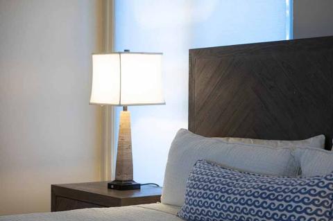 This image shows a bedroom setting featuring a table lamp on a bedside table beside a bed