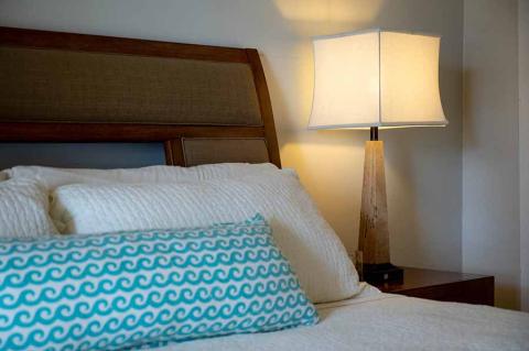 This image shows a neatly arranged bed with a wooden headboard against a wall