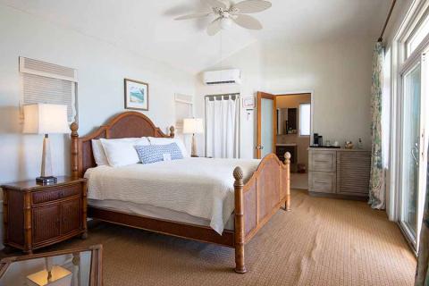 This image shows a well-appointed bedroom featuring a large double bed with a wooden frame and white bedding, complemented by patterned accent pillows