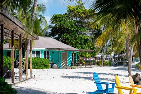 The image shows a serene beachfront scene with a turquoise-colored building that appears to be a tropical resort or beach house