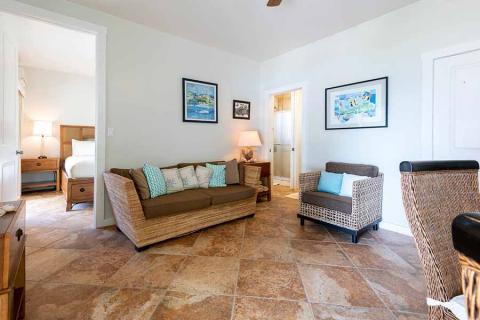 The image displays a well-lit and airy living room leading into a bedroom