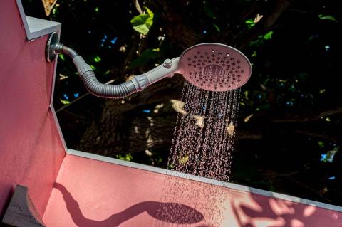 This image features an outdoor shower attached to a pink wall