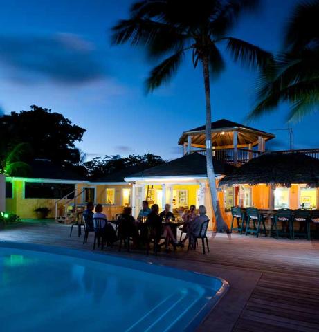 This image features a tropical outdoor setting at dusk with a swimming pool in the foreground