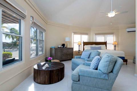 This image displays a well-lit, spacious bedroom with a beach view through multiple windows