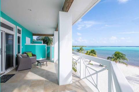 The image shows a beachfront balcony of a house, offering a scenic view of a tropical beach