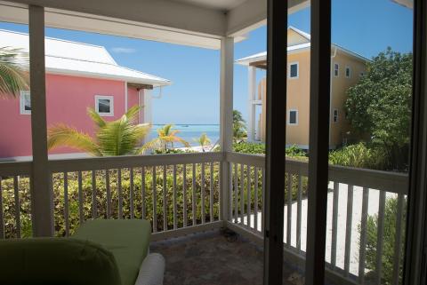 The image shows a view from a balcony or covered patio area, looking out towards a beach scene