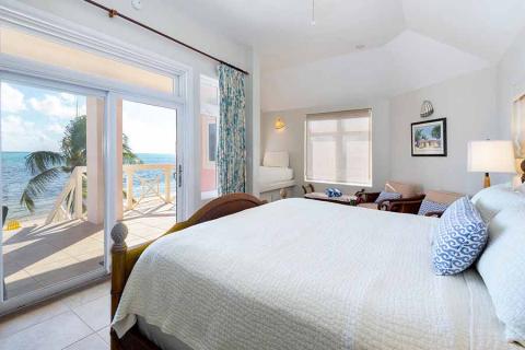This image shows a beautifully appointed bedroom with a large window and glass door leading out to a balcony, which overlooks a stunning beachfront view