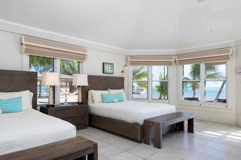 This image shows a spacious and well-lit bedroom with two beds featuring dark wood headboards and placid blue and white bedding