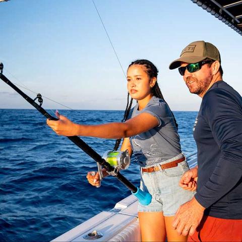 The image shows a young woman and a man engaging in deep-sea fishing from a boat