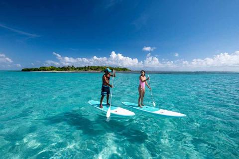 The image features two people on stand up paddleboards over a crystal clear turquoise sea