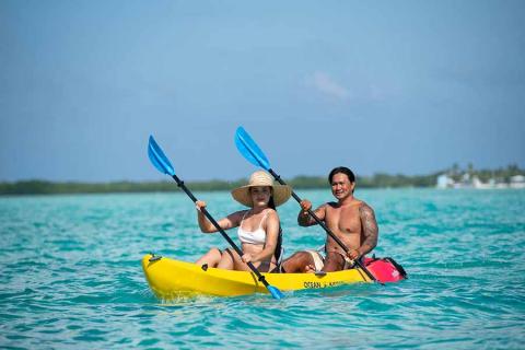 The image shows two people in a yellow kayak on a crystal-clear turquoise sea