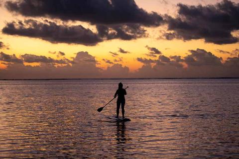 This image shows a person paddleboarding on a calm sea during a beautiful sunset