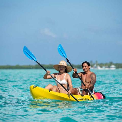 This image features two people kayaking on a calm, clear blue water body