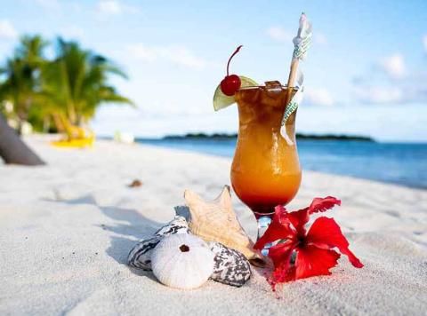 This image features a tropical beach setting with a colorful cocktail in a glass, decorated with a cherry and a straw