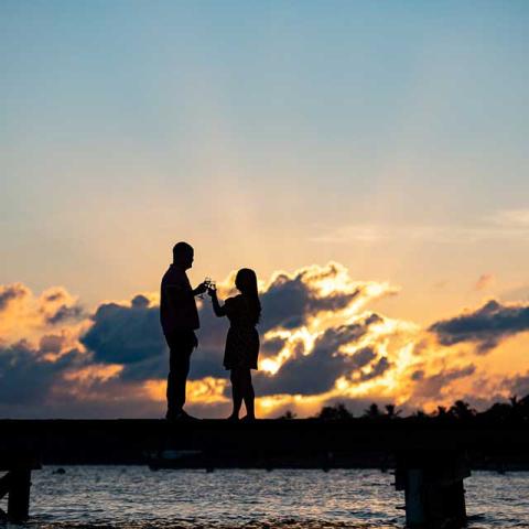 This image features a silhouette of two people standing on a pier during sunset