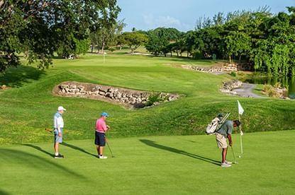 The image shows three people playing golf on a well-maintained golf course