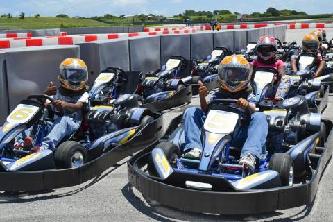 The image shows a group of people sitting in go-karts on a race track, preparing for a kart racing event