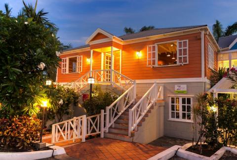 This image depicts a charming and inviting tropical-style building at dusk, warmly illuminated by interior and exterior lights