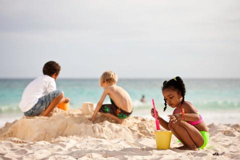 This image features three children playing on a sandy beach