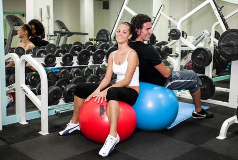 This image shows two individuals seated on exercise balls in a gym setting