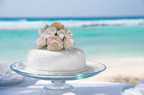 The image features an elegantly decorated cake, possibly a wedding or celebration cake, presented on a glass cake stand