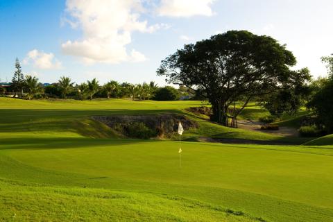 The image shows a beautifully maintained golf course at what appears to be either dawn or dusk, with the sunlight casting soft light across the scene