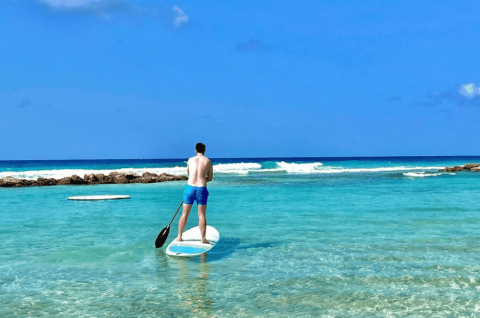This image shows a man paddleboarding on a clear, turquoise water body