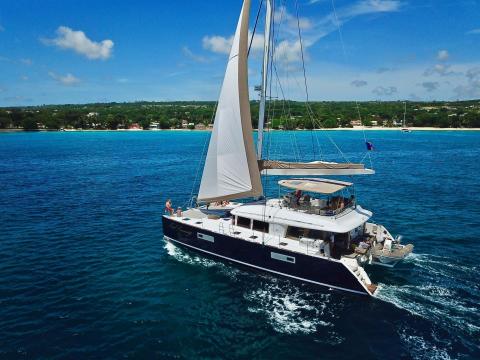 This image shows a large, modern catamaran sailboat cruising on vibrant blue waters