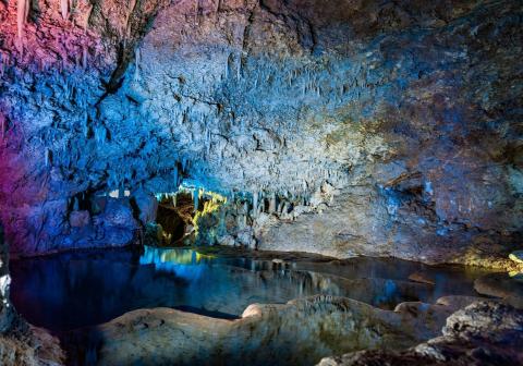 The image shows the beautifully illuminated interior of a cave with a water pool
