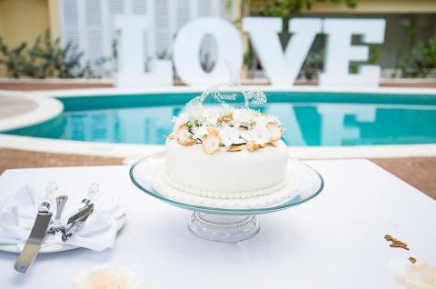 The image features a beautifully decorated wedding cake placed on a glass cake stand
