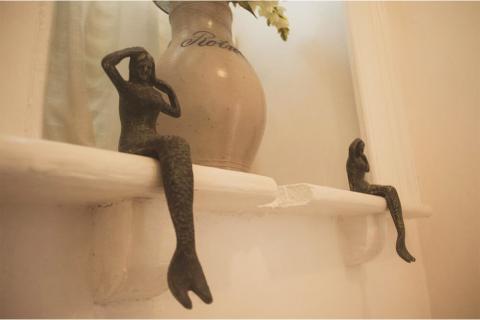 This image showcases two small sculptures of humanoid figures perched on a white shelf