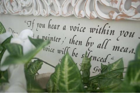 The image shows a decorative white wall with an elegant script text and ornate wood carvings