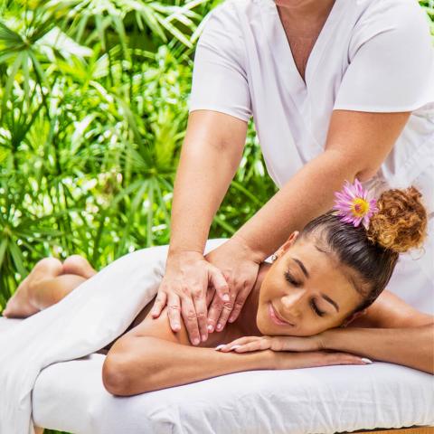 In the image, you see a tranquil scene where a massage therapist in a white uniform is giving a back massage to a woman lying face down on a massage table