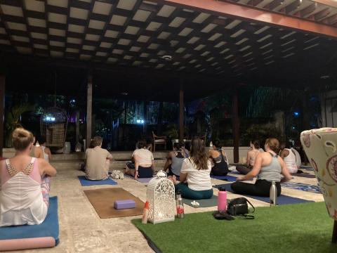 The image shows a group of people participating in a yoga session during the evening or night