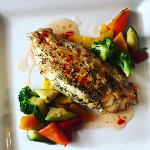 The image shows a plate of food consisting of a grilled chicken breast seasoned with herbs and spices, accompanied by a variety of cooked vegetables