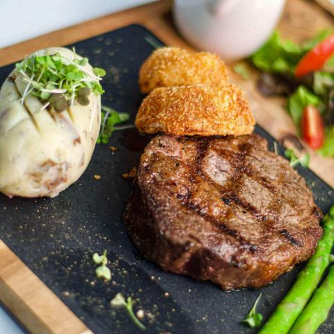 This image features a deliciously plated meal consisting of a grilled steak with clear grill marks, two golden-brown breaded items that could be croquettes, and a large potato topped with microgreens