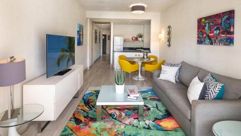 This image shows a modern and colorful living room interior that transitions into a dining area