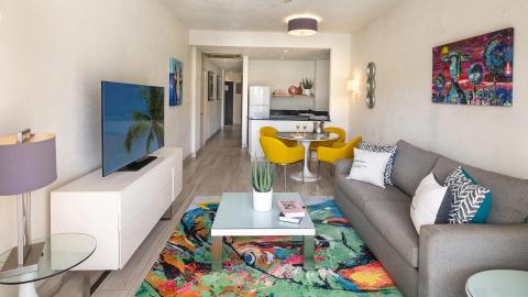This image shows a modern and stylishly decorated apartment living room that flows into a kitchen and dining area