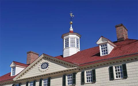 The image features a classic colonial-style building with an elegant red brick roof and a white wooden cupola topped by a weathervane