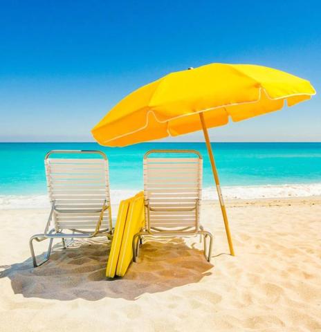 This image features a scenic beach view with two white lounge chairs under a bright yellow umbrella